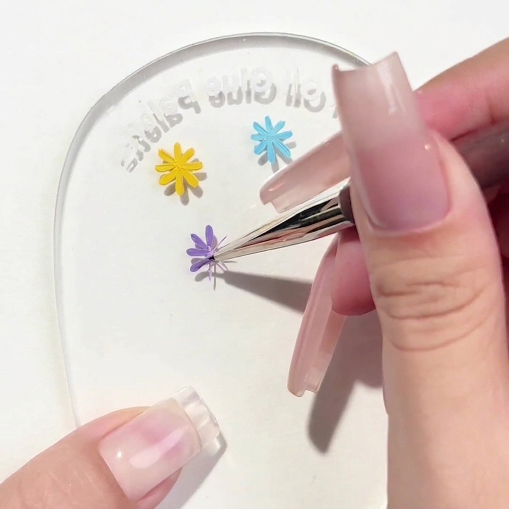 A liner brush applying a third purple petal to the daisy design on the palette.