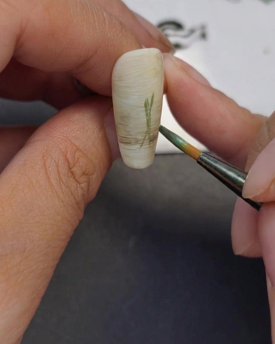 Close-up of a fine liner brush drawing thin green lines on a nail to represent flower stems.