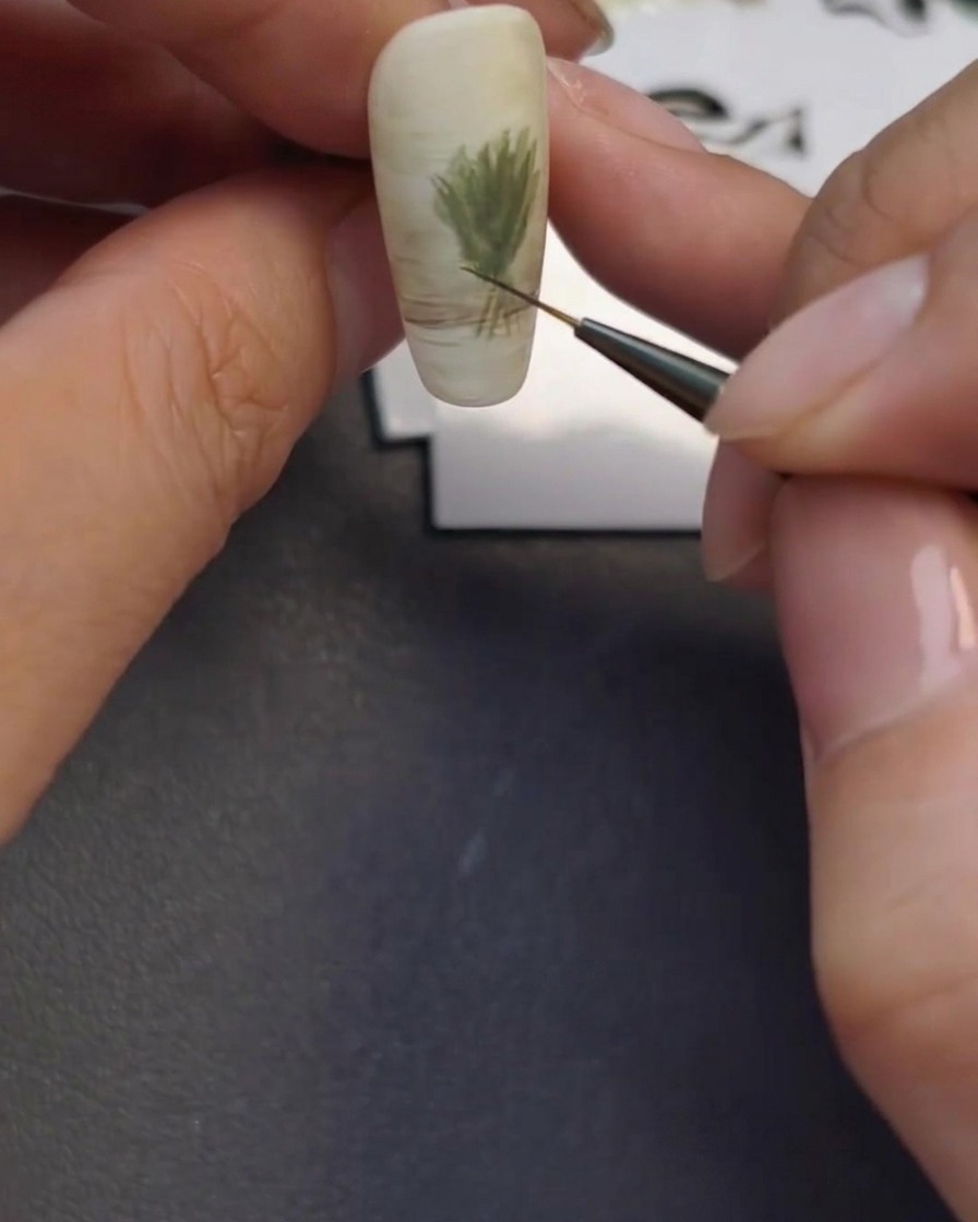 A fine liner brush creating the faint outline of a glass vase at the base of the nail art design.