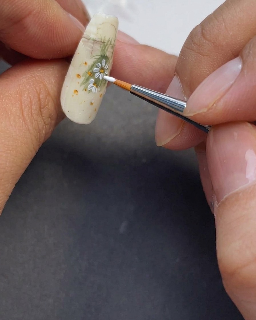 Close-up of more white petals being painted onto the nail to complete the daisy design.