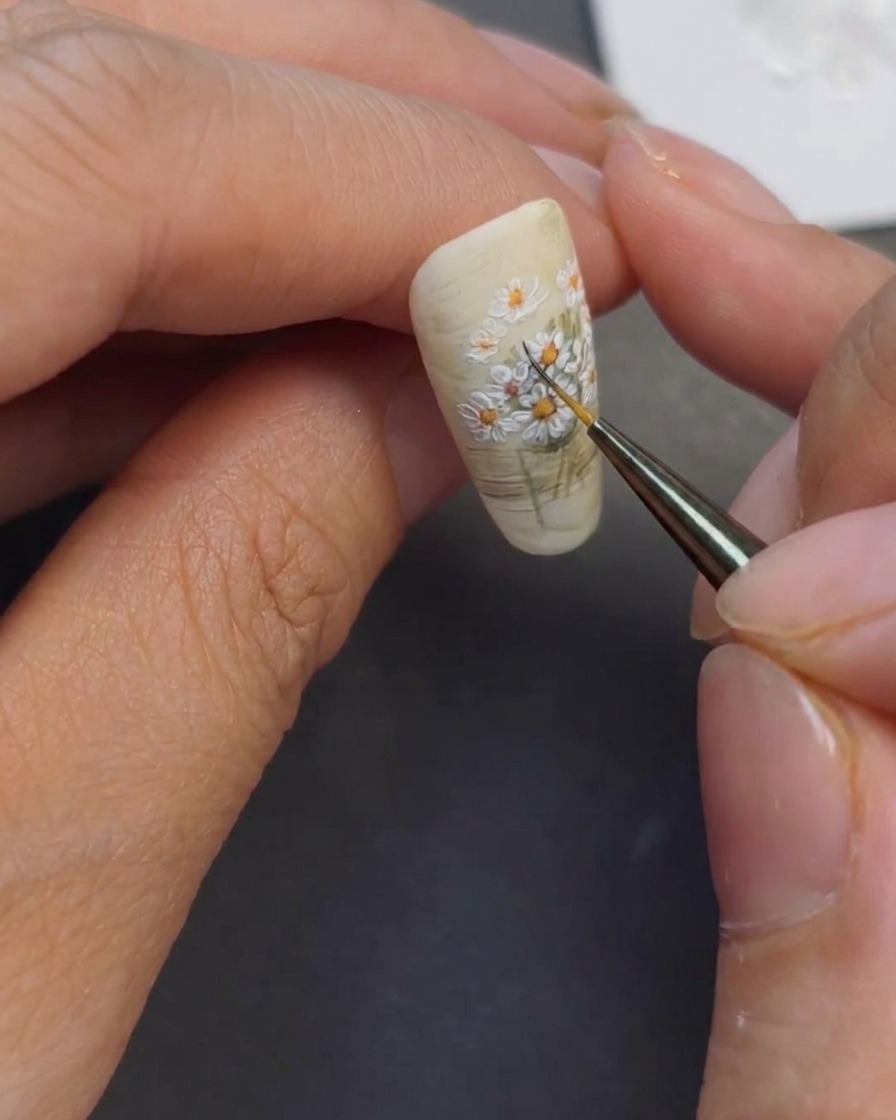 A close-up view of a detail brush adding dark green lines to the stems of the painted daisy bouquet.