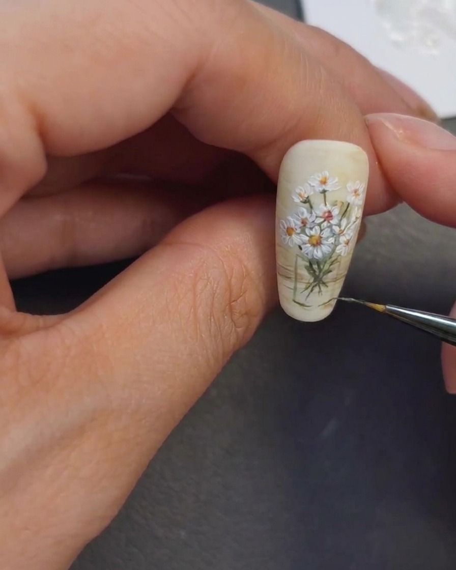 A nail artist applying thin, light highlights over the painted vase area to create a glass-like effect.