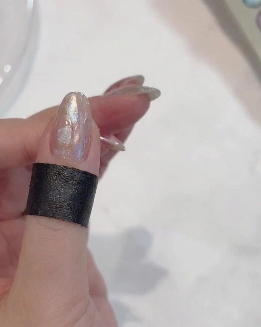 A hand holding the nail under a UV lamp to cure the painted flower design.
