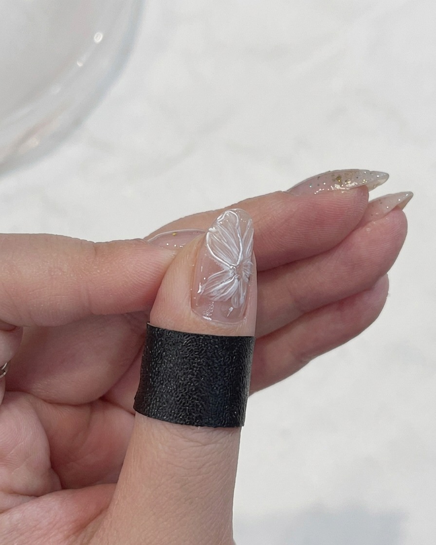 A fine liner brush tracing the delicate edges of white flower petals on a nail.