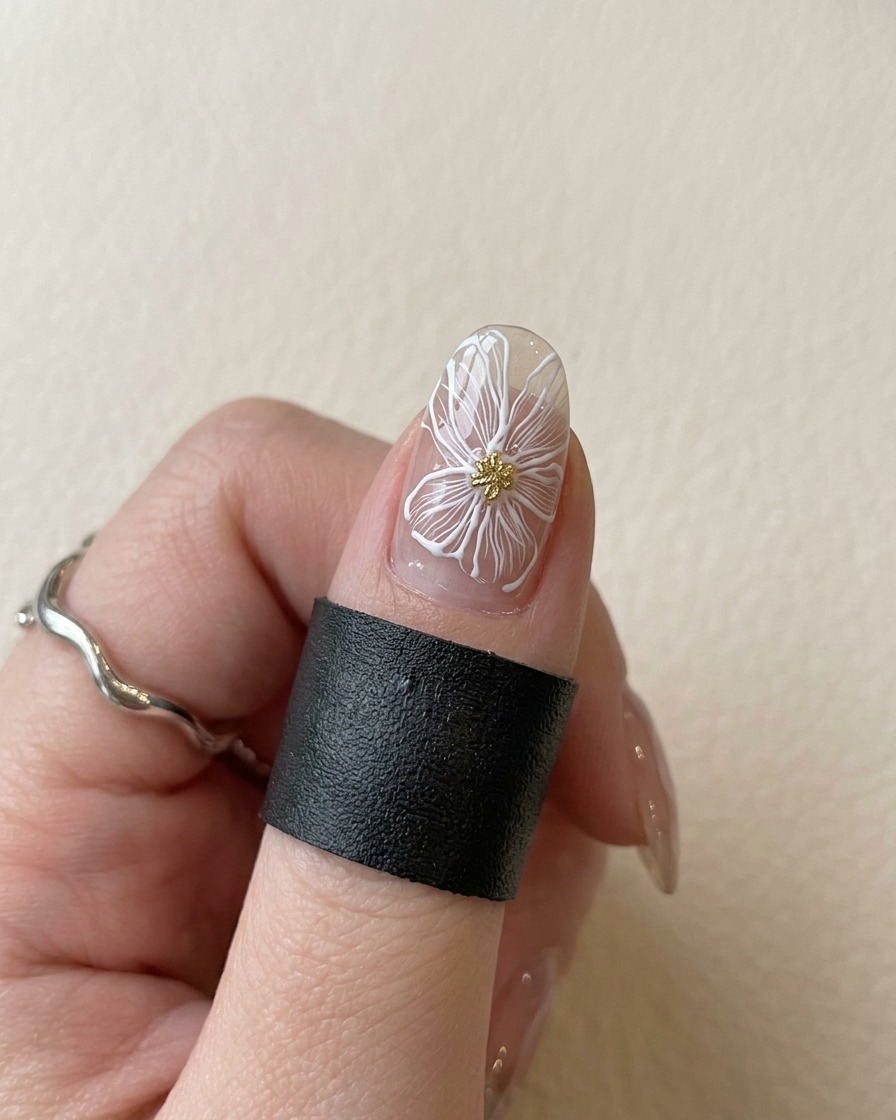A fingernail with a white flower and gold center placed under a violet UV lamp to cure.