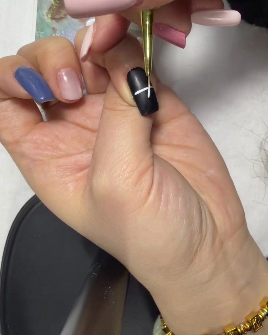 A close-up showing a white cross shape formed by intersecting horizontal and vertical lines on a black nail.