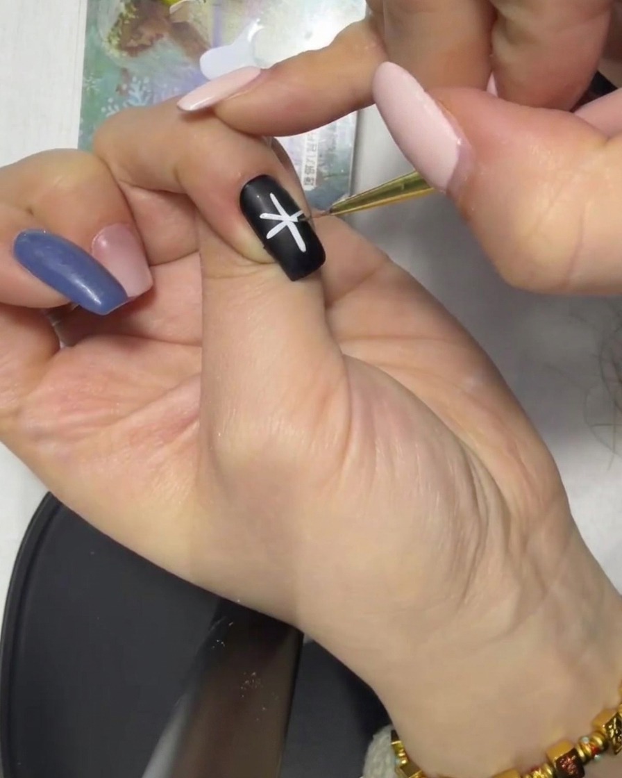 A close-up of a completed white asterisk-shaped design centered on a black nail.