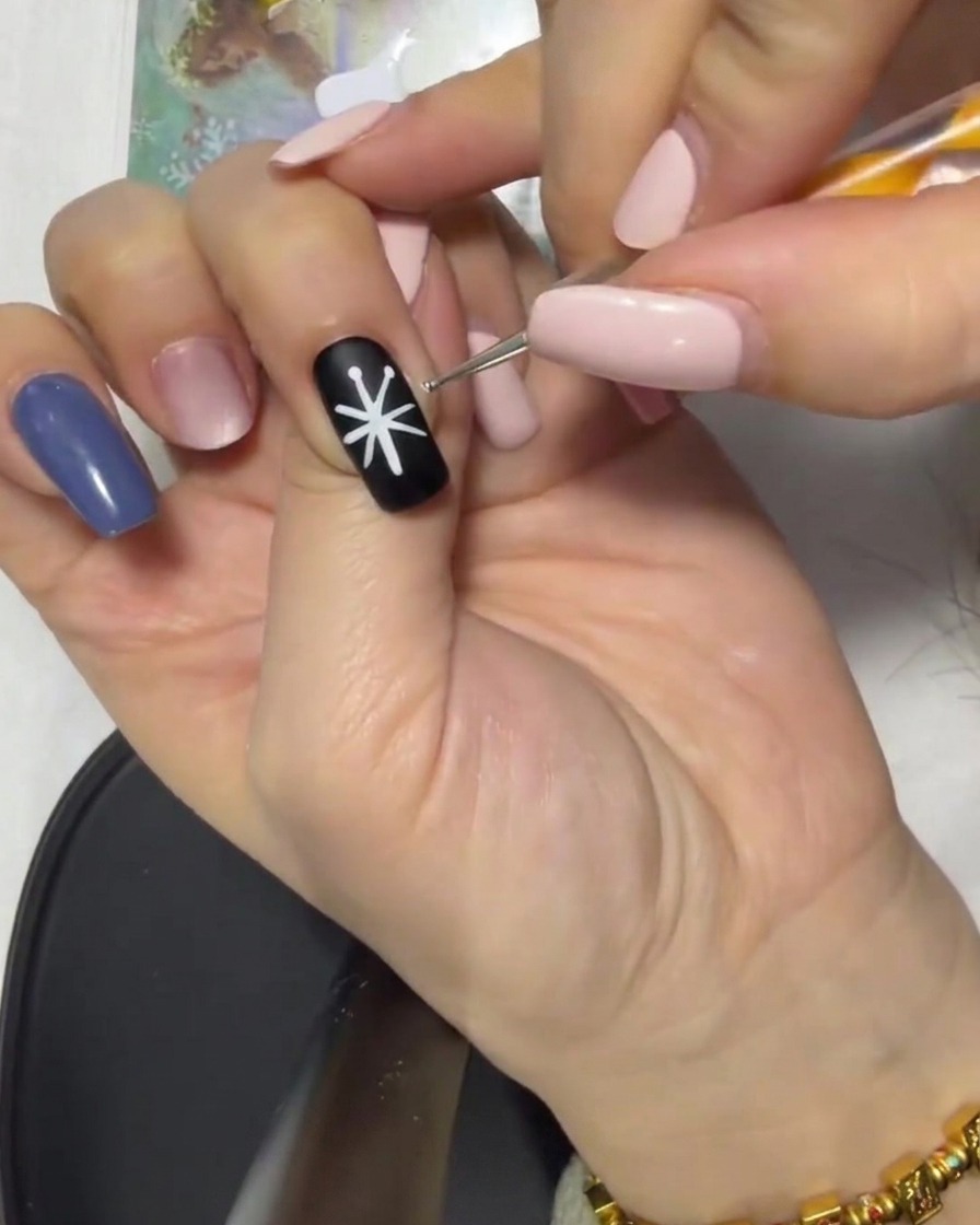 A close-up of a black nail with a white star-like guide being connected from the tips to the center with a liner brush.