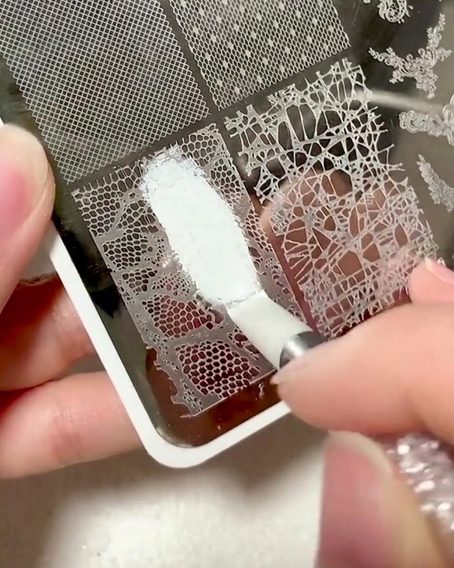 A plastic scraper being used to clear excess gel from a lace stamping plate.