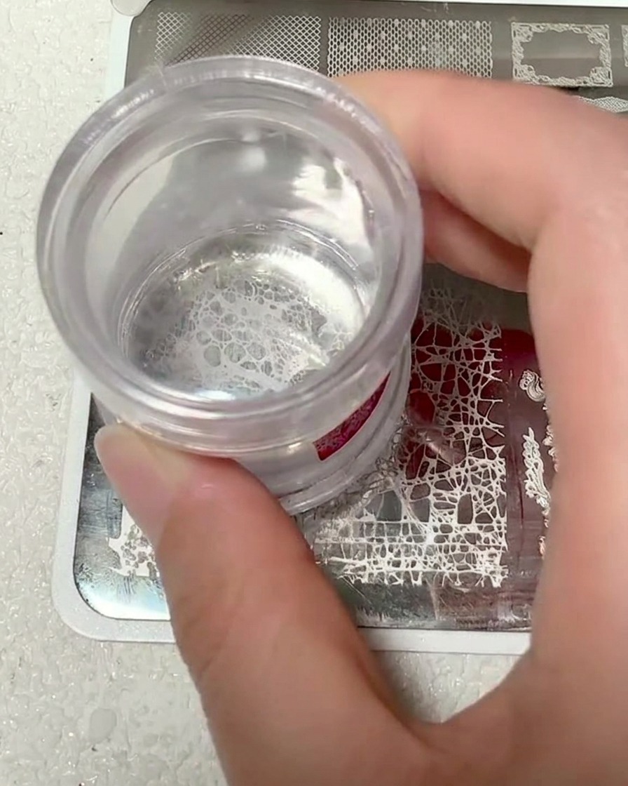 A clear silicone stamper head showing the picked-up white lace pattern.