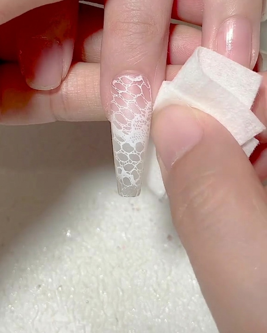 A sponge being used to tidy up the edges of a newly stamped lace design on a nail.