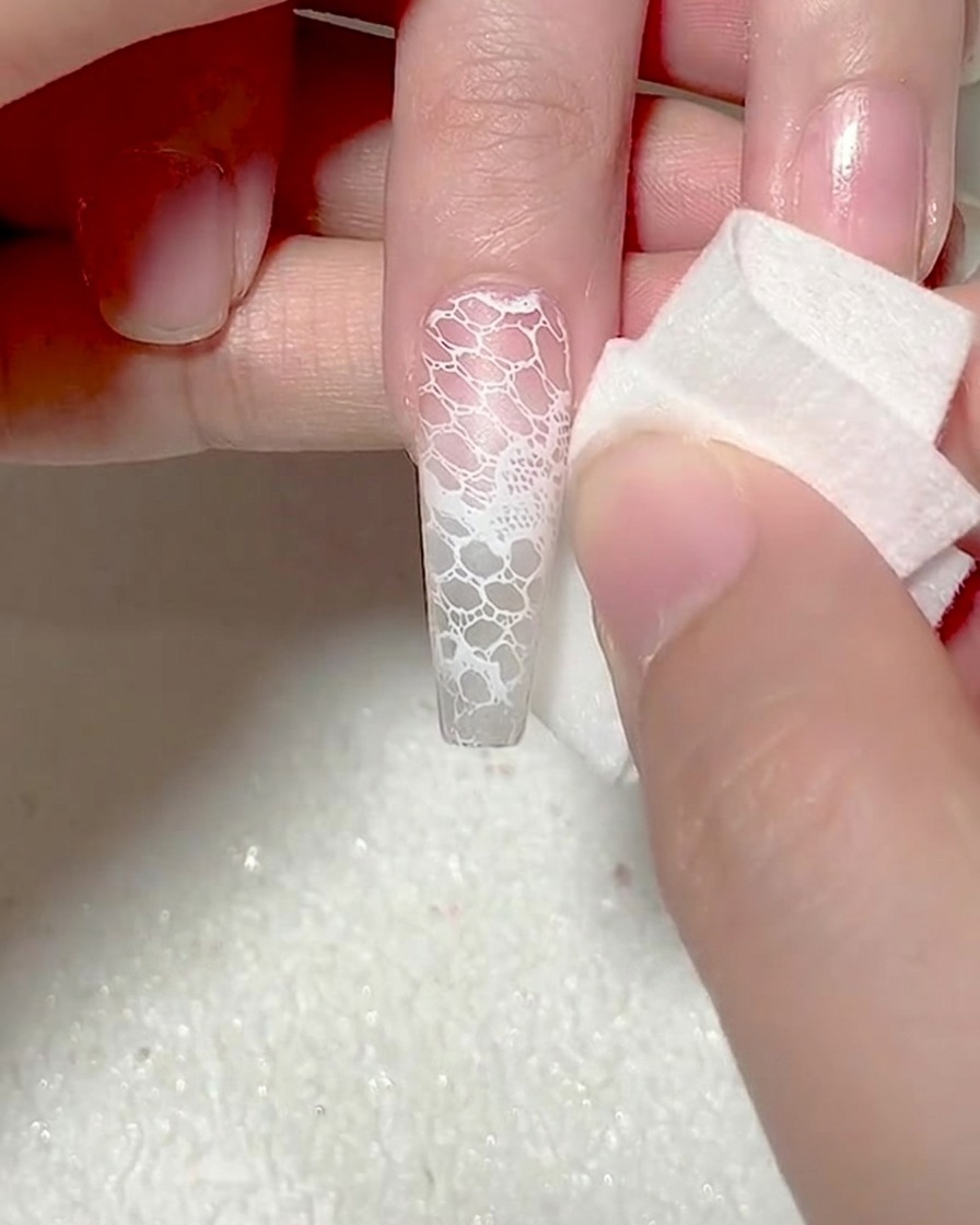 A close-up of a white makeup sponge dabbing white gel onto the tip of a nail to create an ombre effect.