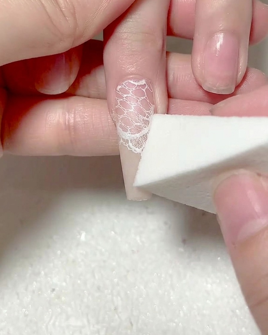 A makeup sponge patting a second layer of white gel onto the tip of the nail.
