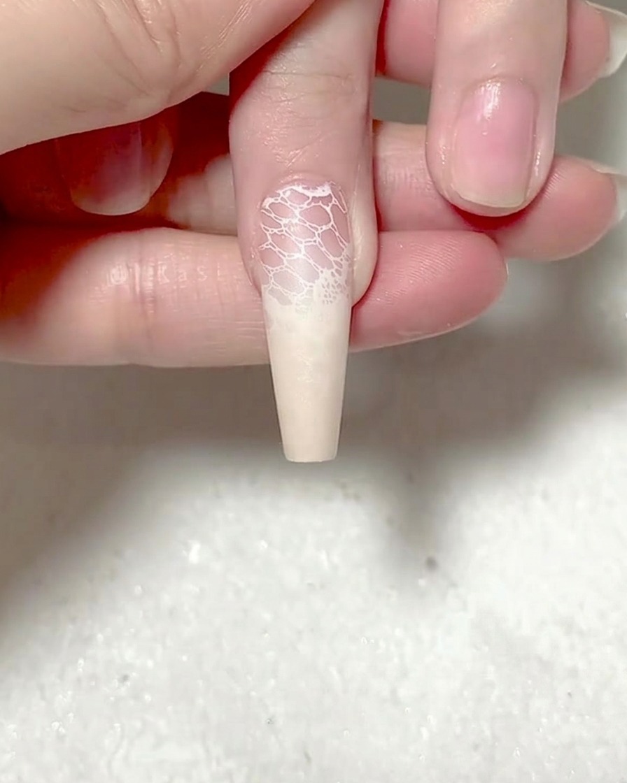 A pair of tweezers placing a detailed red rose sticker onto the surface of a nail.