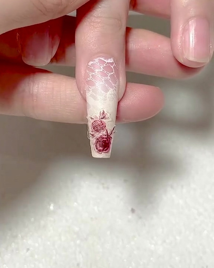 A silicone-tipped tool pressing down firmly on a red rose nail sticker.