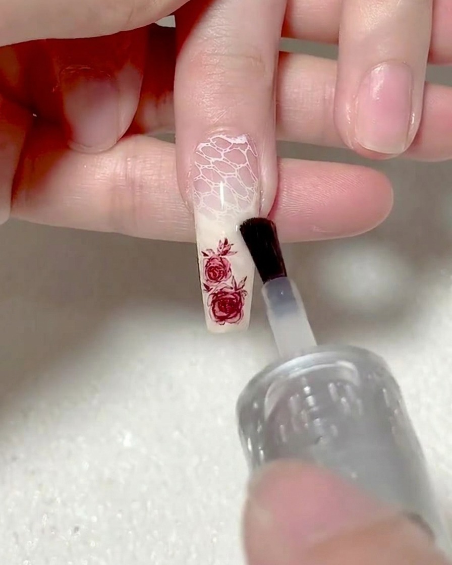 A brush applying clear base gel over a rose sticker to encapsulate it.