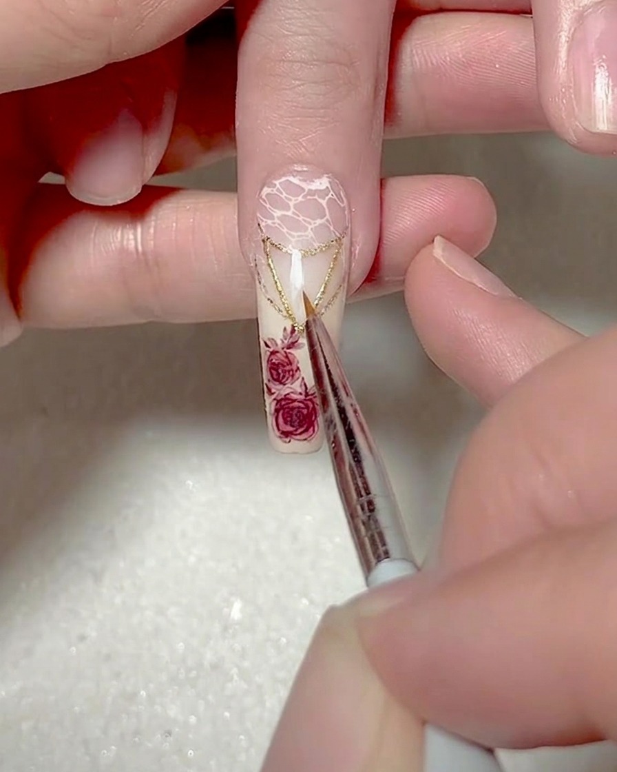 A close-up of a fine liner brush painting a small, precise white gel triangle on the tip of the nail.