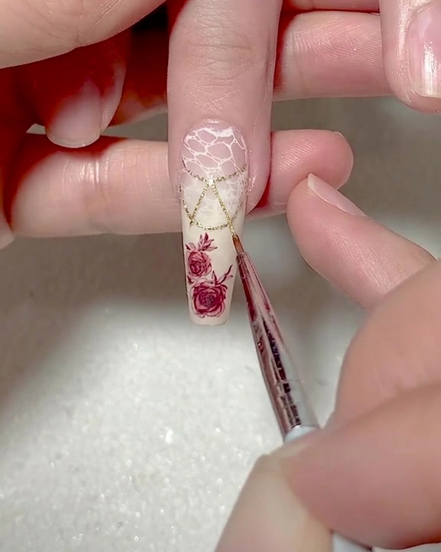 A close-up of a fine liner brush adding white gel outlines along the edges of a triangle design on a nail.