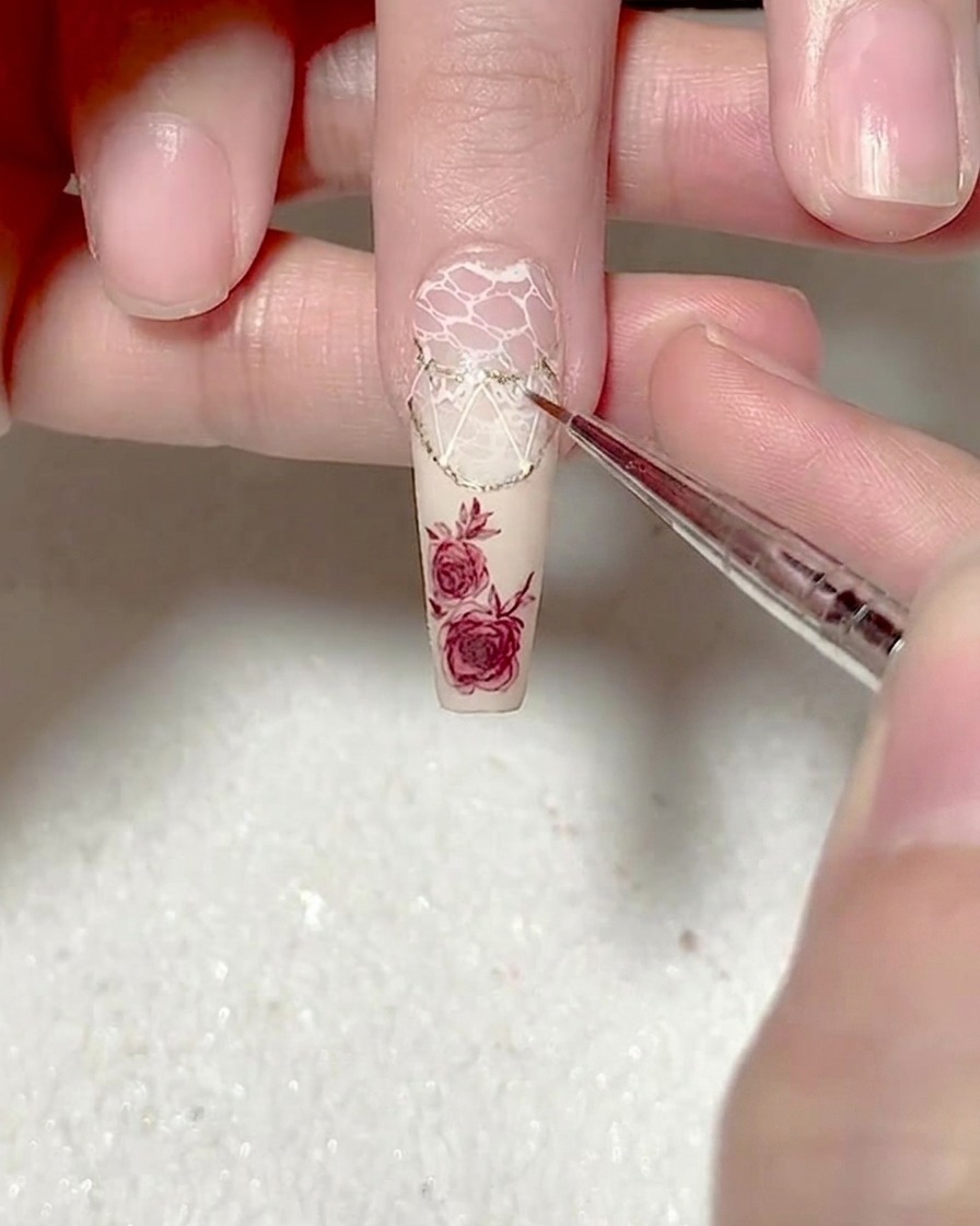 A close-up of a liner brush adding small, intricate white lace patterns to the existing geometric design on the nail.