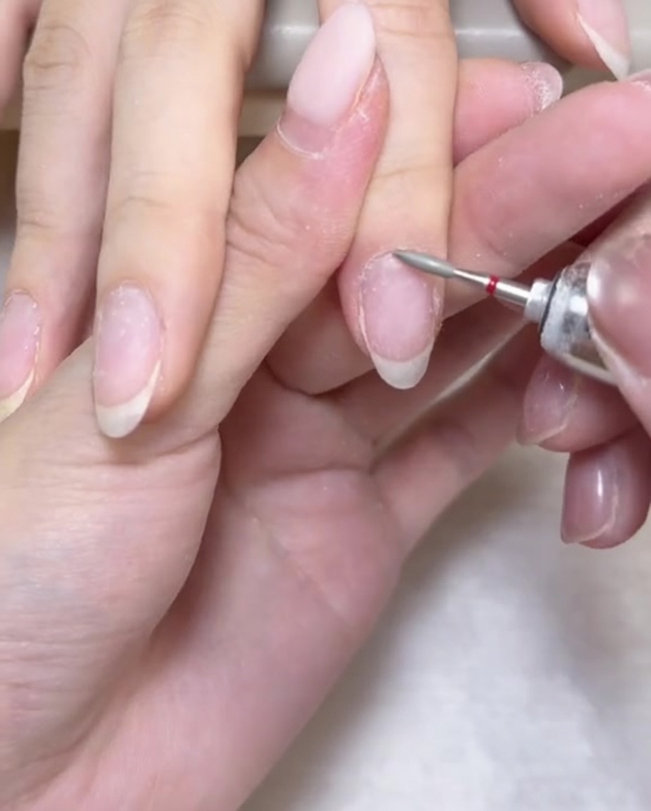 An e-file drill bit being used to gently clear and open the cuticle area around the base of the nail.