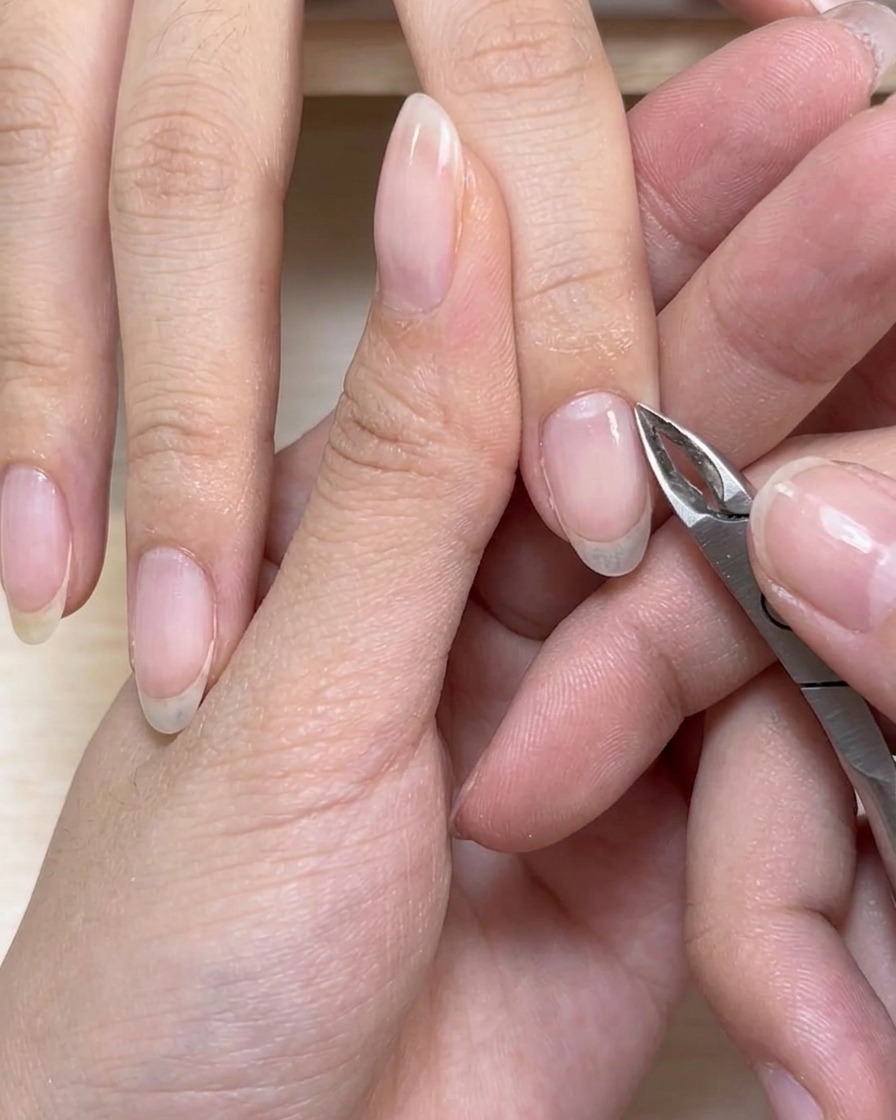 Cuticle nippers carefully trimming excess dead skin around the base of a fingernail.