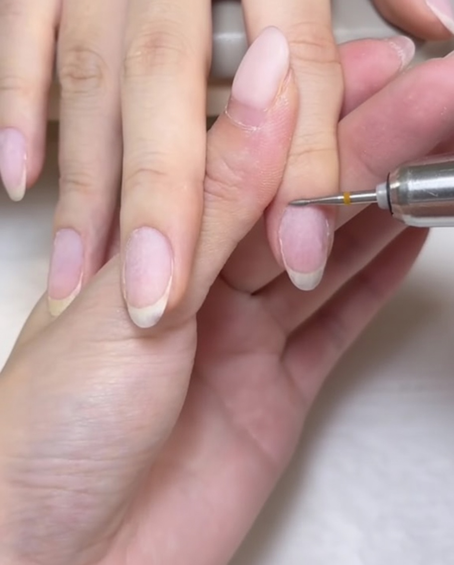 A small, rounded millet-shaped drill bit being used to precisely clean the cuticle area of the nail.