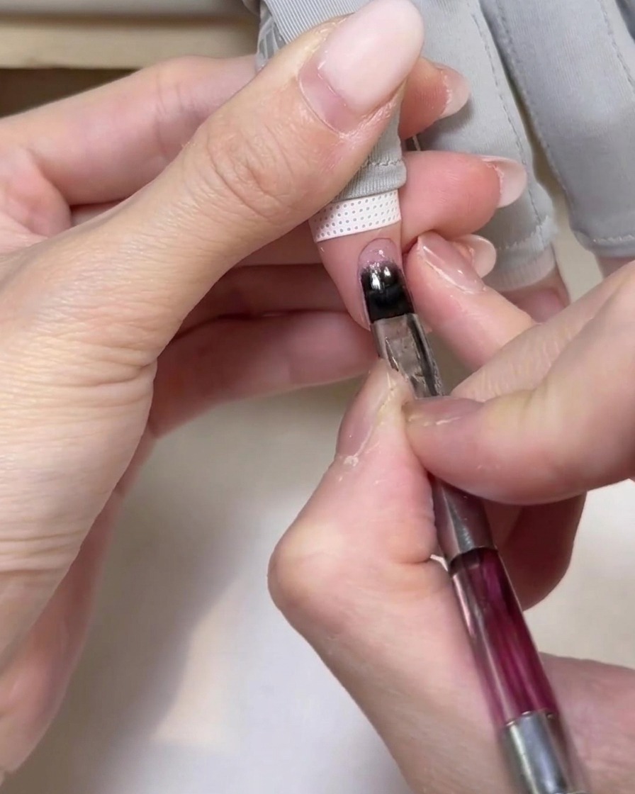 A hand positioned inside a portable UV lamp, with the nails receiving light to cure the base gel.