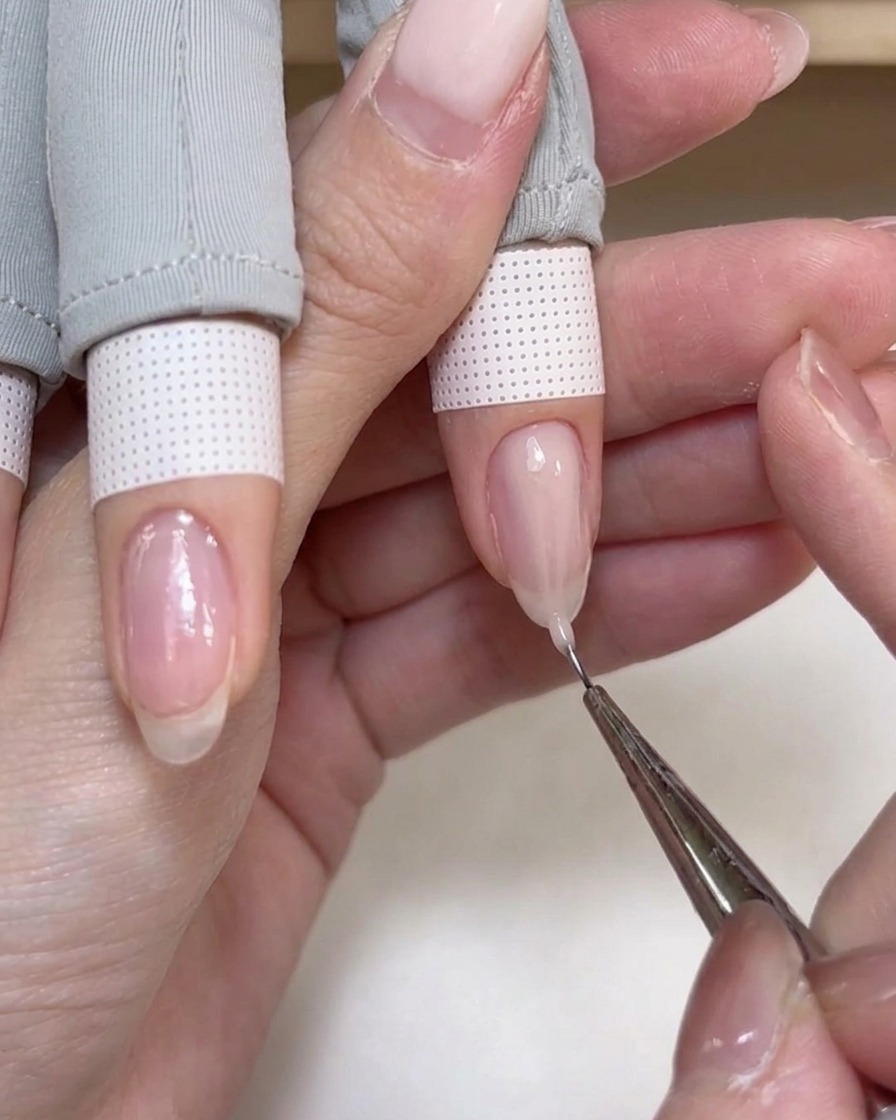 A fine liner brush dragging a bead of soft pink builder gel toward the tip of the nail.