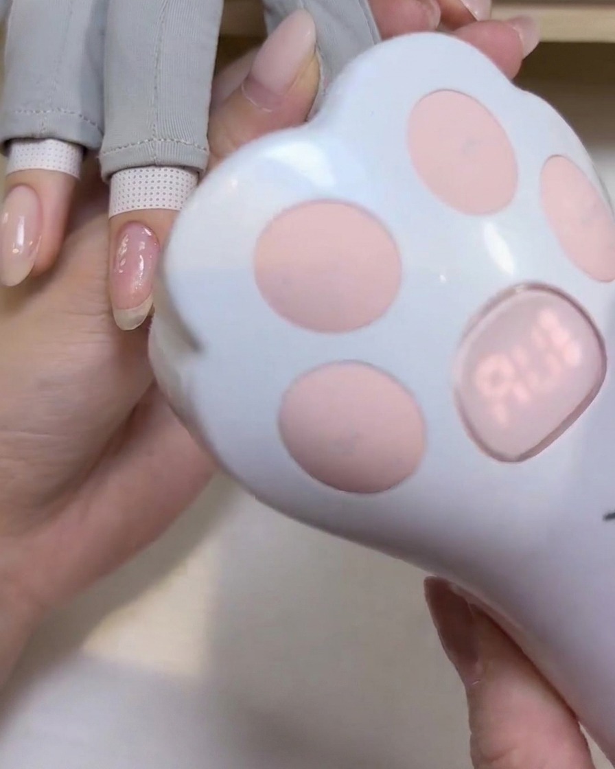 A cute cat-paw shaped handheld UV/LED lamp positioned over a fingernail to cure the gel polish.
