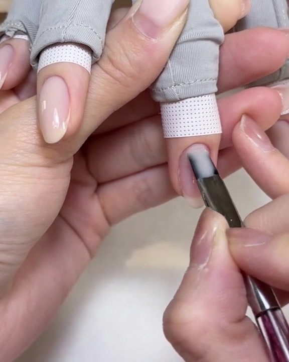 A flat gel brush applying a smooth layer of clear transfer gel over a pink builder gel nail.