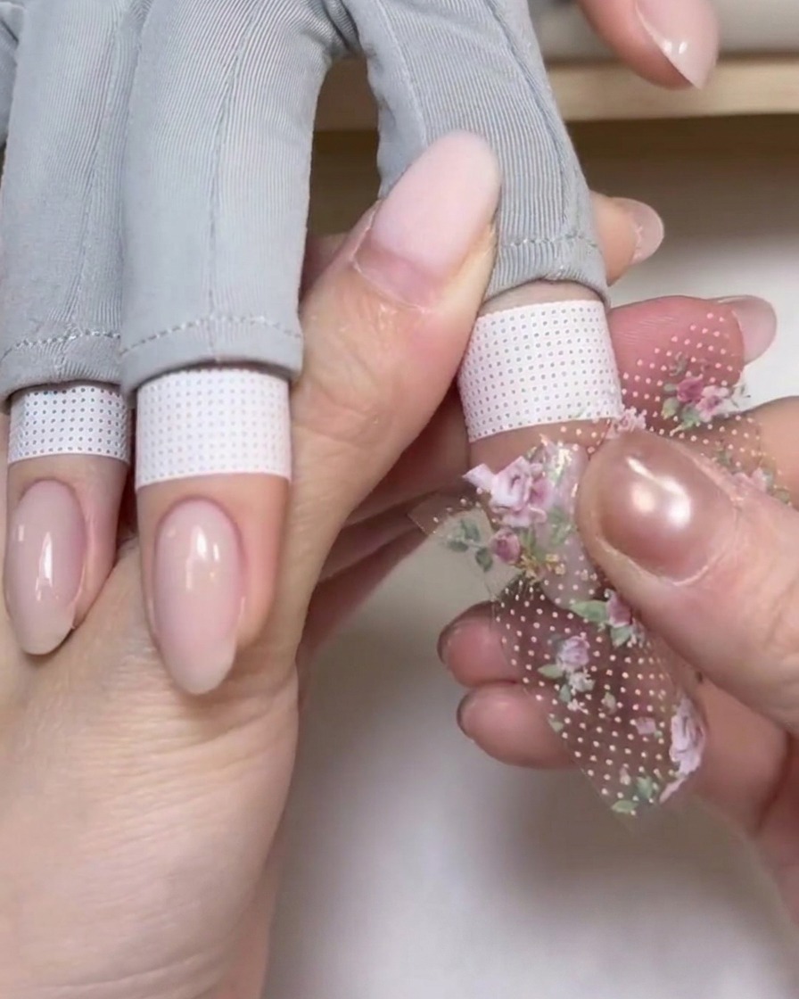 A piece of rose-patterned foil being pressed firmly onto the nail surface with a fingertip.