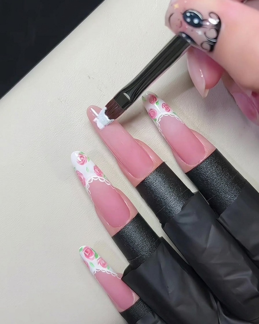 A flat gel brush painting a thick white French tip onto the edge of a nude pink fingernail.cite: 1