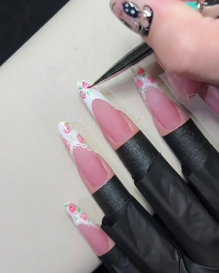 A fine liner brush swirling pink gel into wet white gel on a French tip to create tiny rose patterns.cite: 1