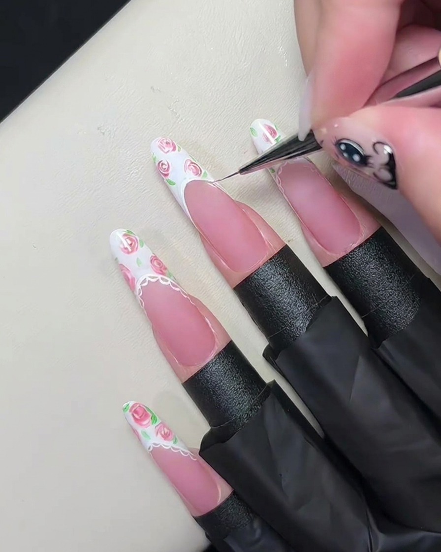 A close-up macro shot of a fine liner brush tracing a thin white line along the smile line of a French manicure.