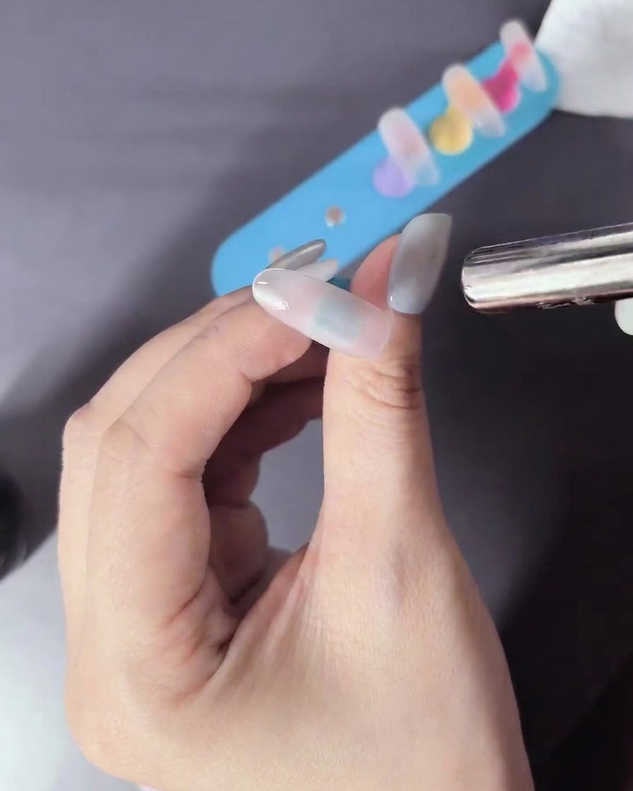 A magnetic tool being held near the nail to pull metallic particles into a design.