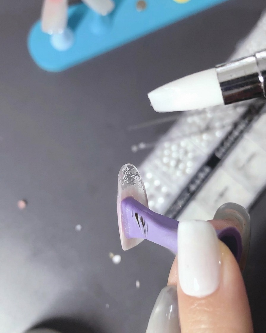 A brush applying a small amount of clear bead gel onto the surface of the cured nail.
