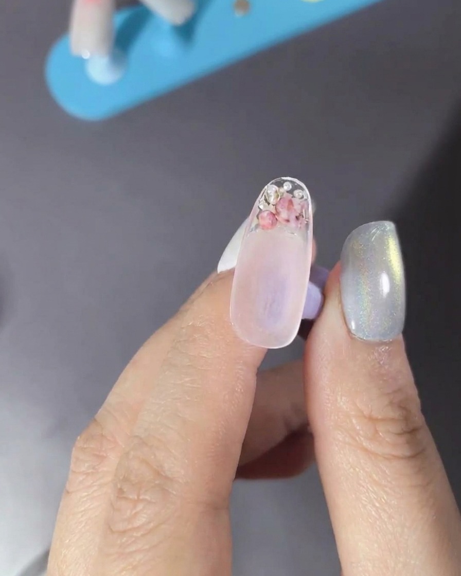 A brush applying a clear top coat over a nail decorated with flowers and pearls.