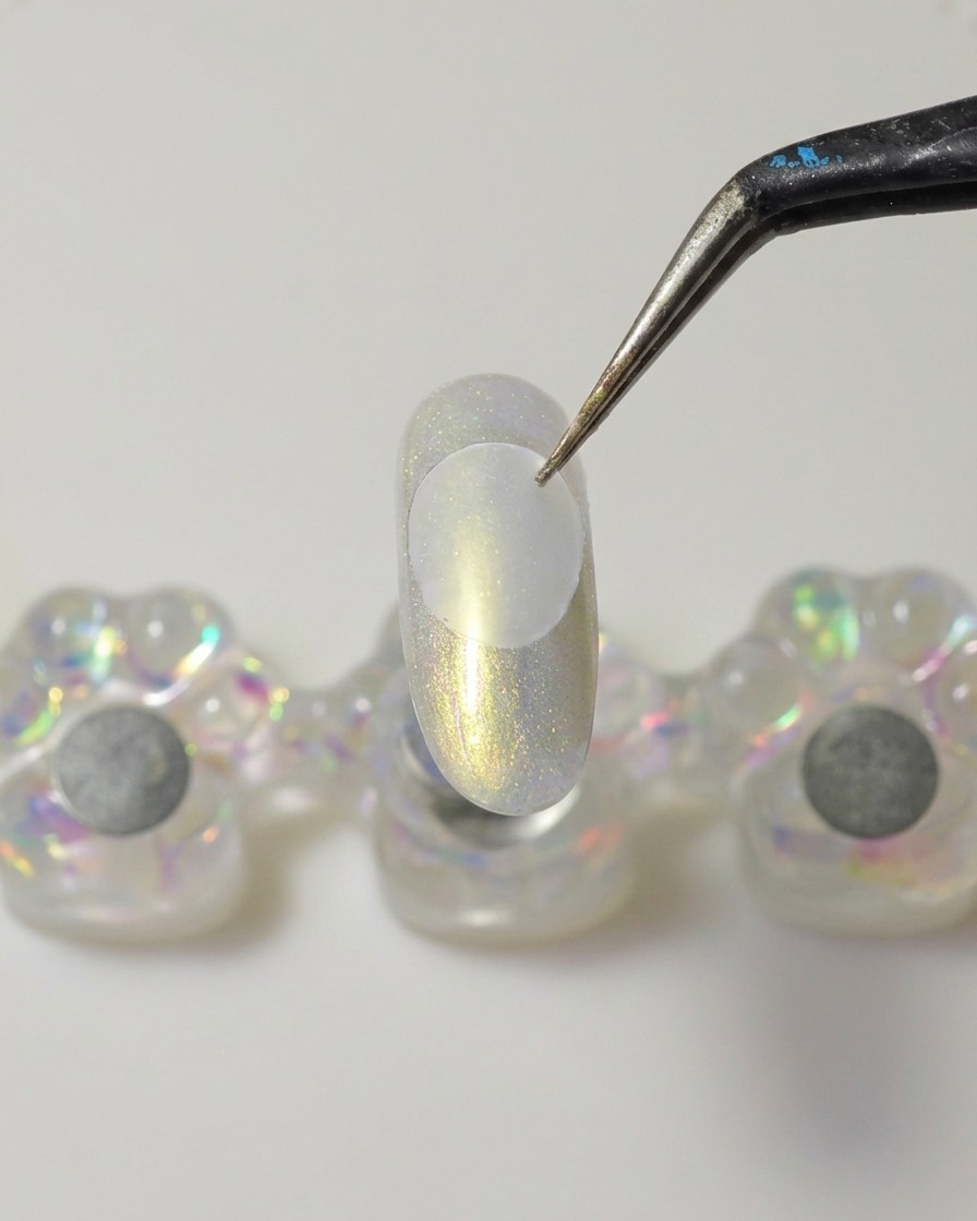 A metal spatula applying a dollop of thick, clear solid builder gel onto the underside of a clear plastic disc.
