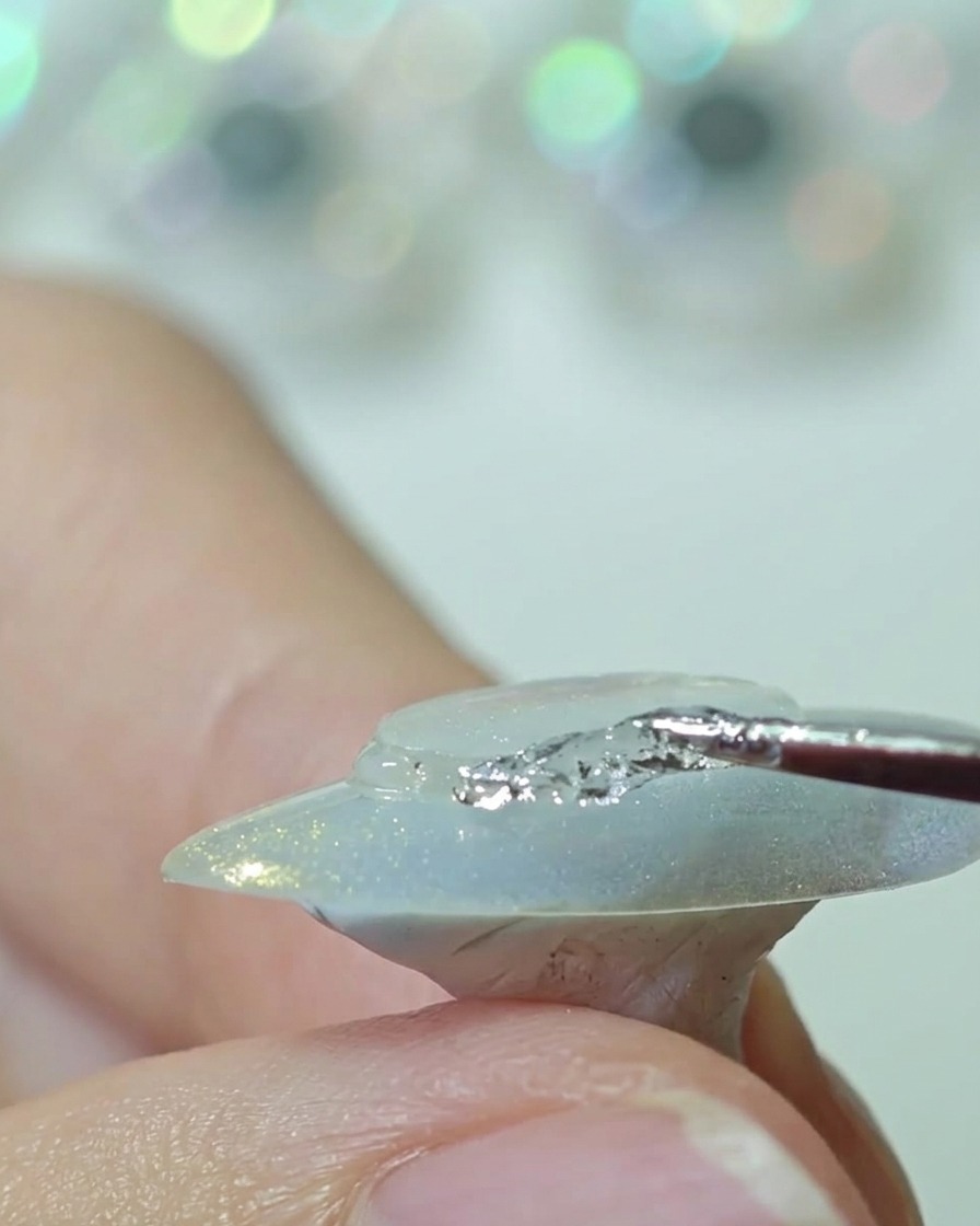 A silicone tool pressing down a clear plastic disc onto the center of a nail, smoothing the edges.