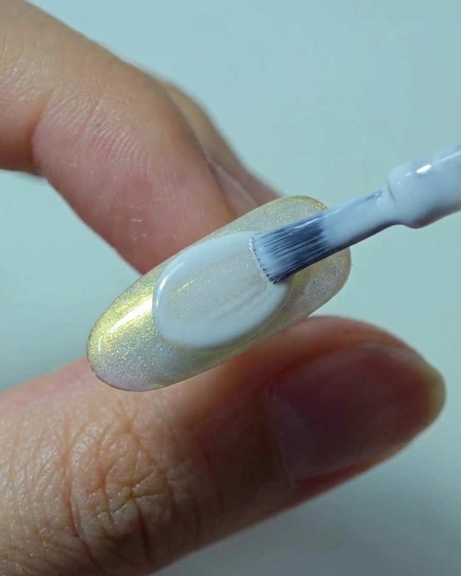 A brush applying a smooth, opaque second layer of white gel polish over the nail.