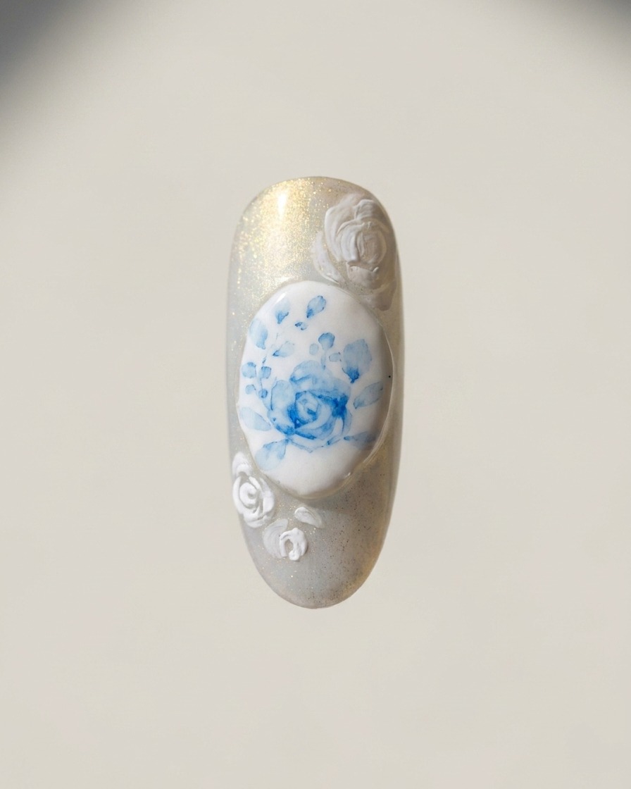 A fine liner brush painting white rose outlines on the edges of the nail surrounding the central blue rose design.