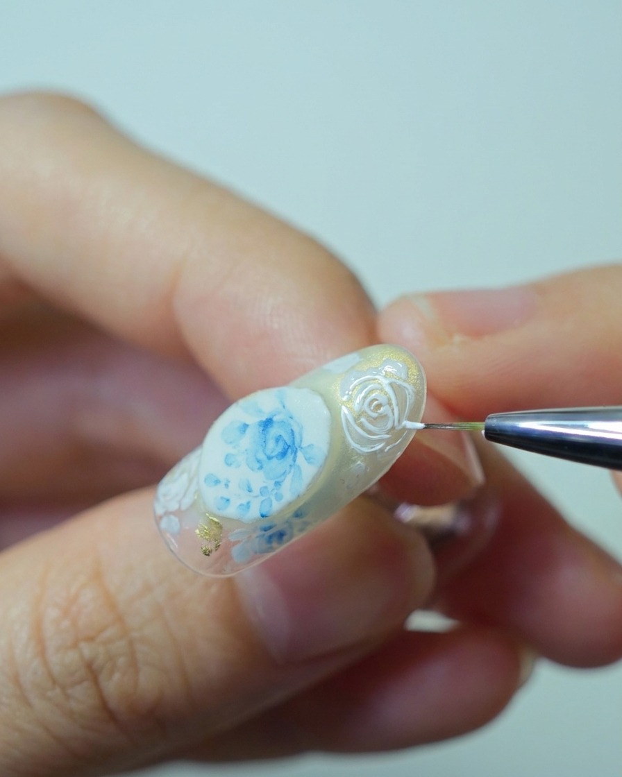 Close-up of a brush applying thick white relief gel over the previously painted rose outlines to build 3D texture.