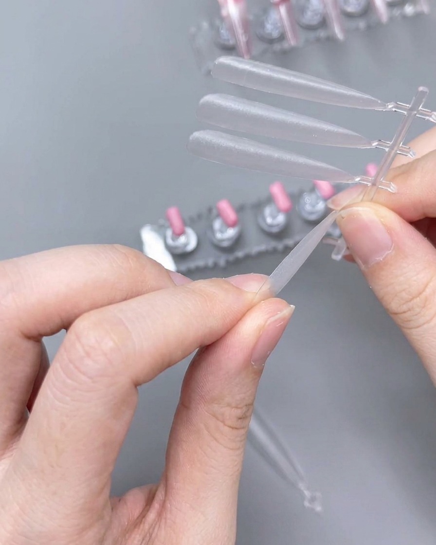 A close-up of hands using a hand file to shape the edge of a clear plastic nail tip.