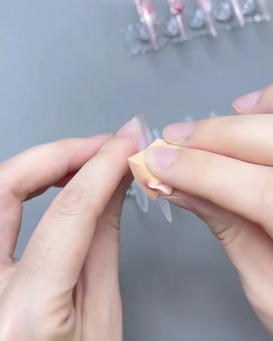 A brush blending sheer pink gel on the nail tip to create an ombre gradient.