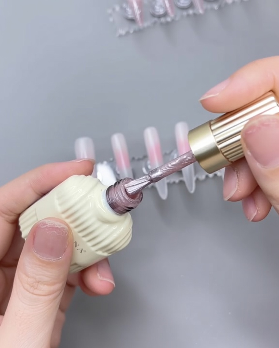 A nail brush applying pink cat-eye gel over a cured sheer pink base on a nail tip.