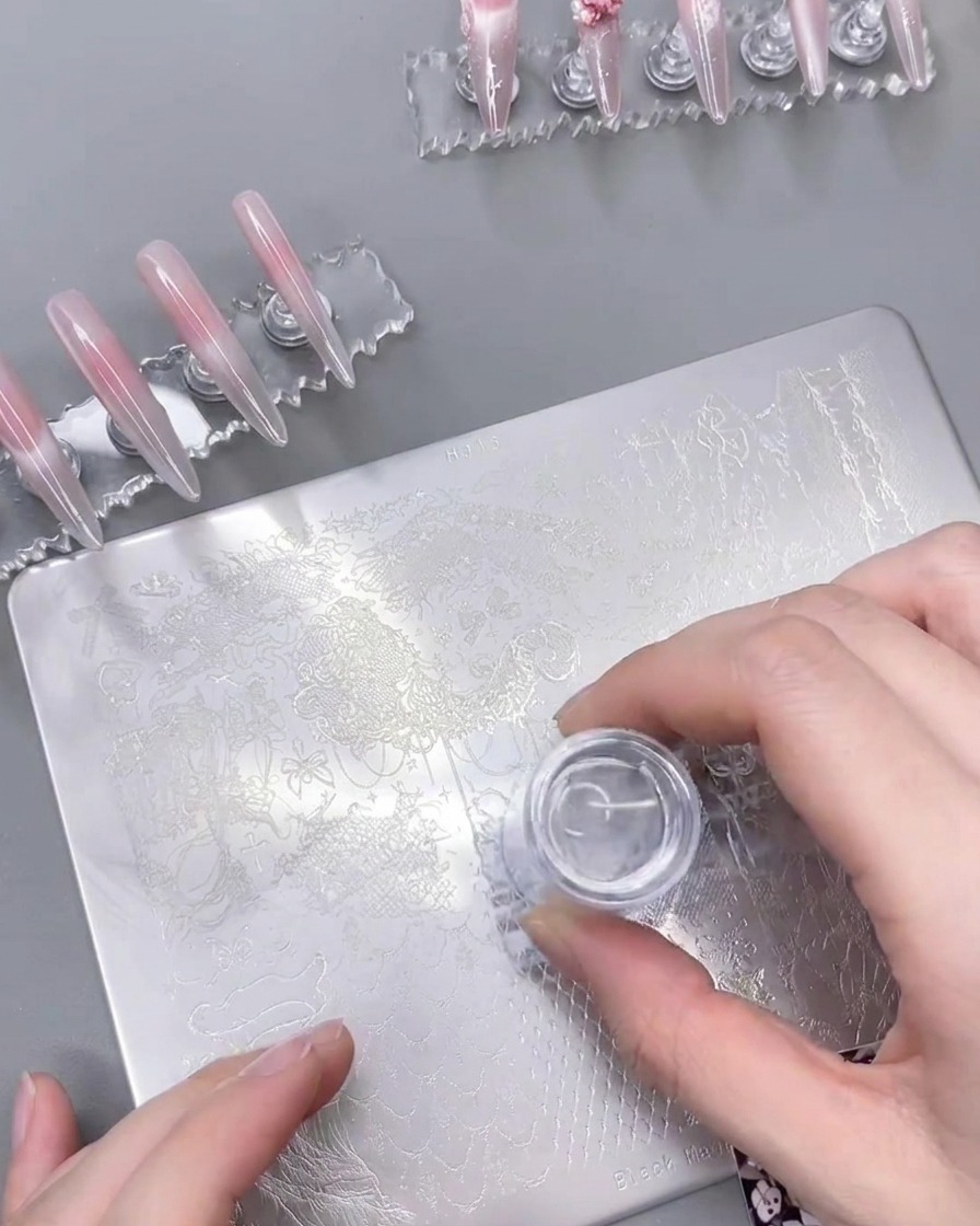 A clear silicone nail stamper pressed onto a steel stamping plate, successfully lifting the white lace design.