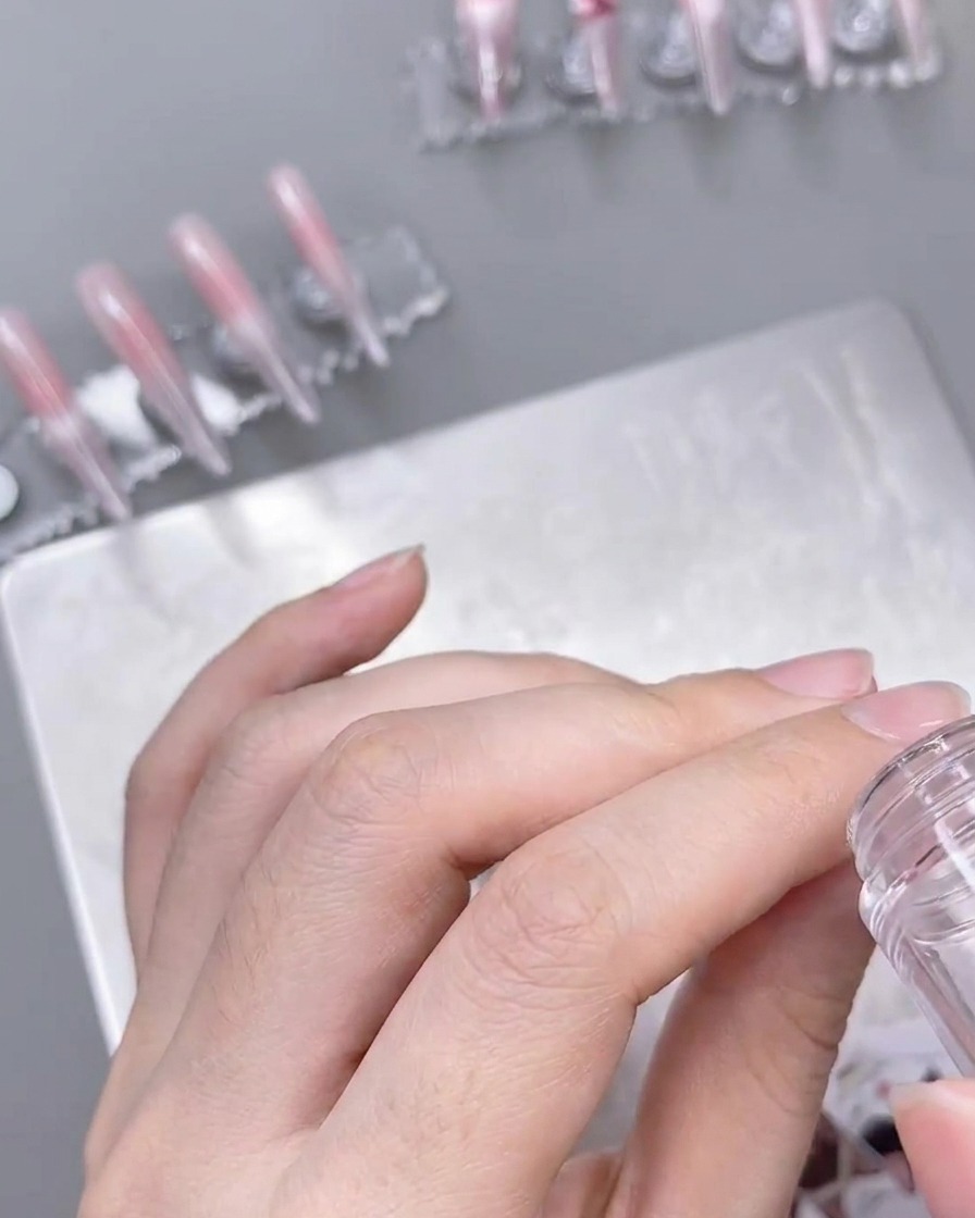 A clear stamper applying a delicate white lace pattern onto a prepped, ombre-colored nail.