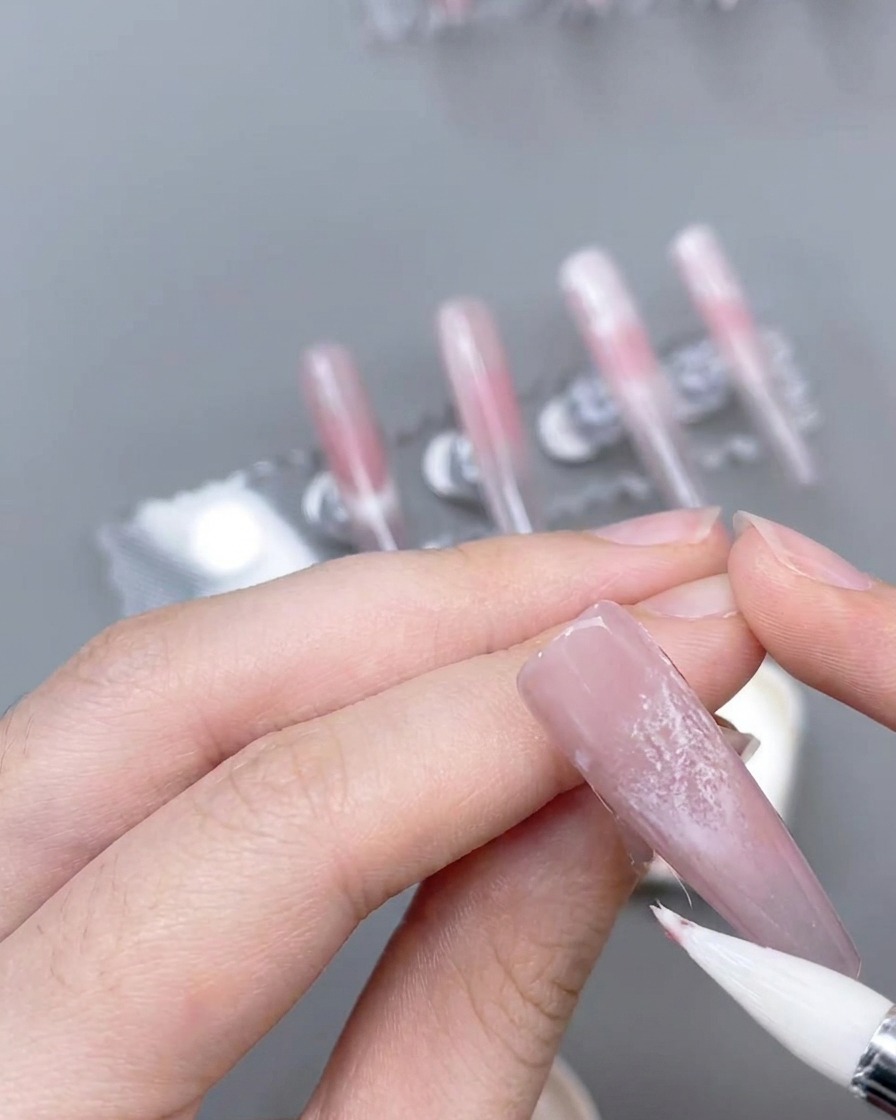 A fine liner brush creating thin, precise pink accent lines over a decorated nail.