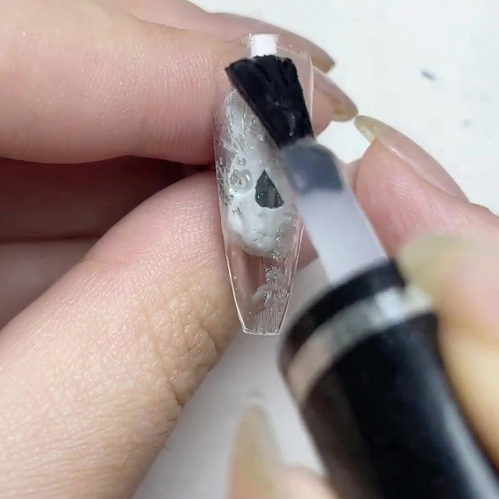 A brush applying a coat of matte top over the silver foiled nail.