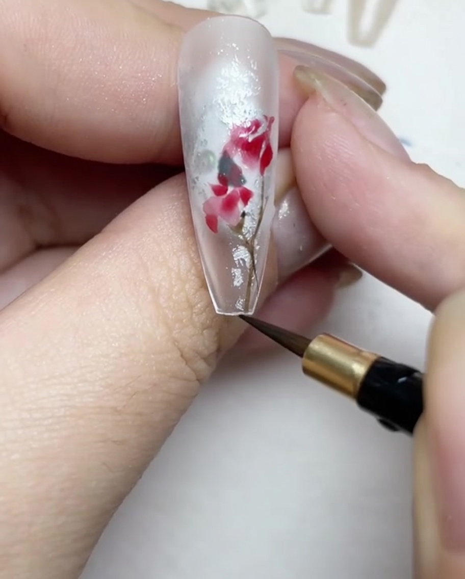 Drawing fine brown and green stems and leaves around the rose design.